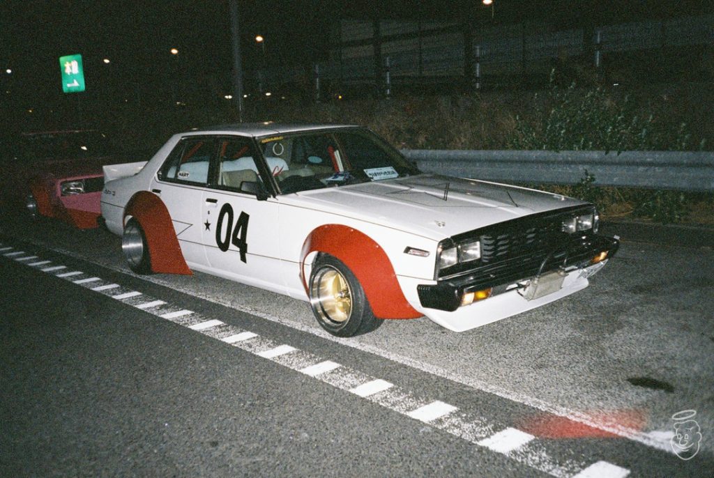 White and red retro car with number 04 parked on a Japanese road at night.