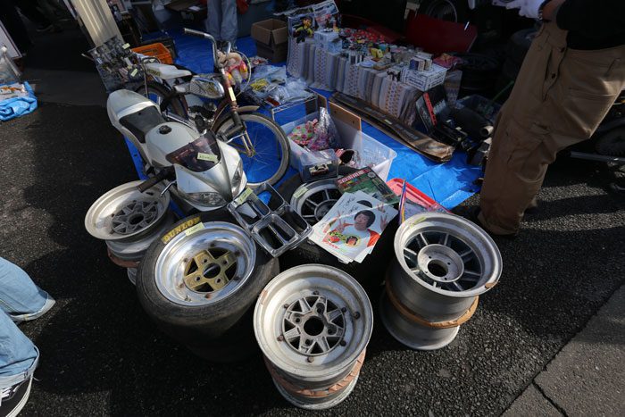 Market stall with motorcycle, alloy wheels, and various items for sale in Japan.