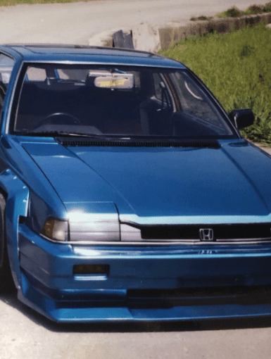 Modified blue Honda with wide body kit and TRUST sticker on windshield parked on a road.