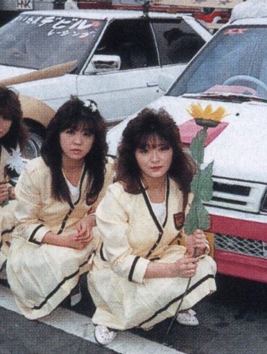 Three women in uniforms holding flowers in front of decorated cars in a Japanese car show. レディース on car windshield.Explanation:
The alt text describes the main elements in the image including the women, their uniforms, the flowers they are holding, and the Japanese car show setting to ensure it is relevant and improves SEO.