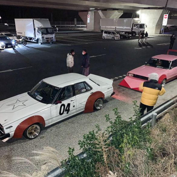 Vintage Japanese modified cars parked under an overpass at night with people standing nearby.
