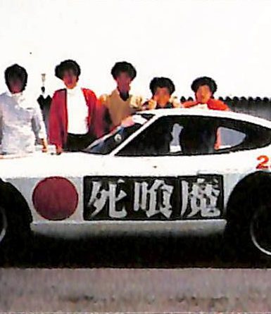 A white sports car with Shinigami and 2998cc written on it, and six people posing behind it on a sunny day.