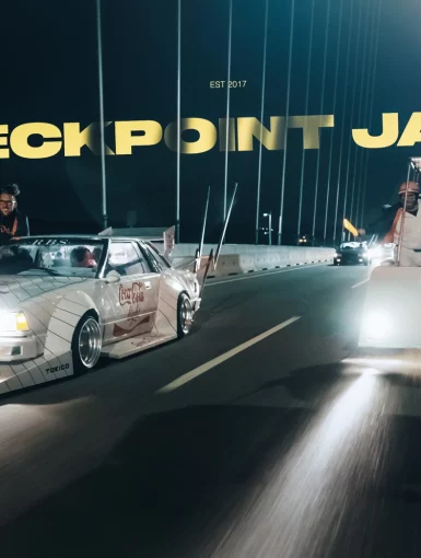 Vintage cars on a Japanese bridge at night with the text Checkpoint Japan.