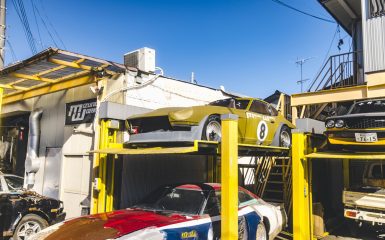Vintage racing cars at Izumo Works garage in Japan on a sunny day. The sign reads Izumo Works (イズモワークス).