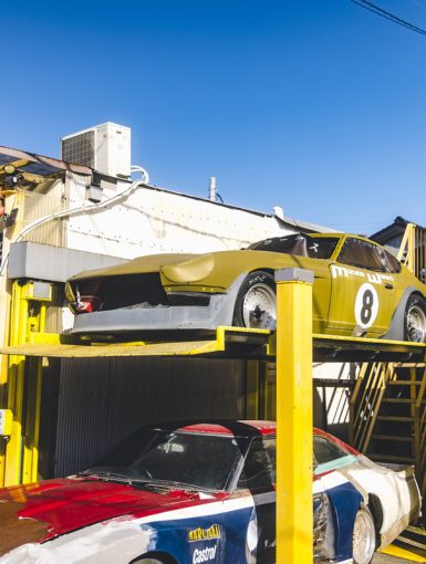 Vintage racing cars at Izumo Works garage in Japan on a sunny day. The sign reads Izumo Works (イズモワークス).