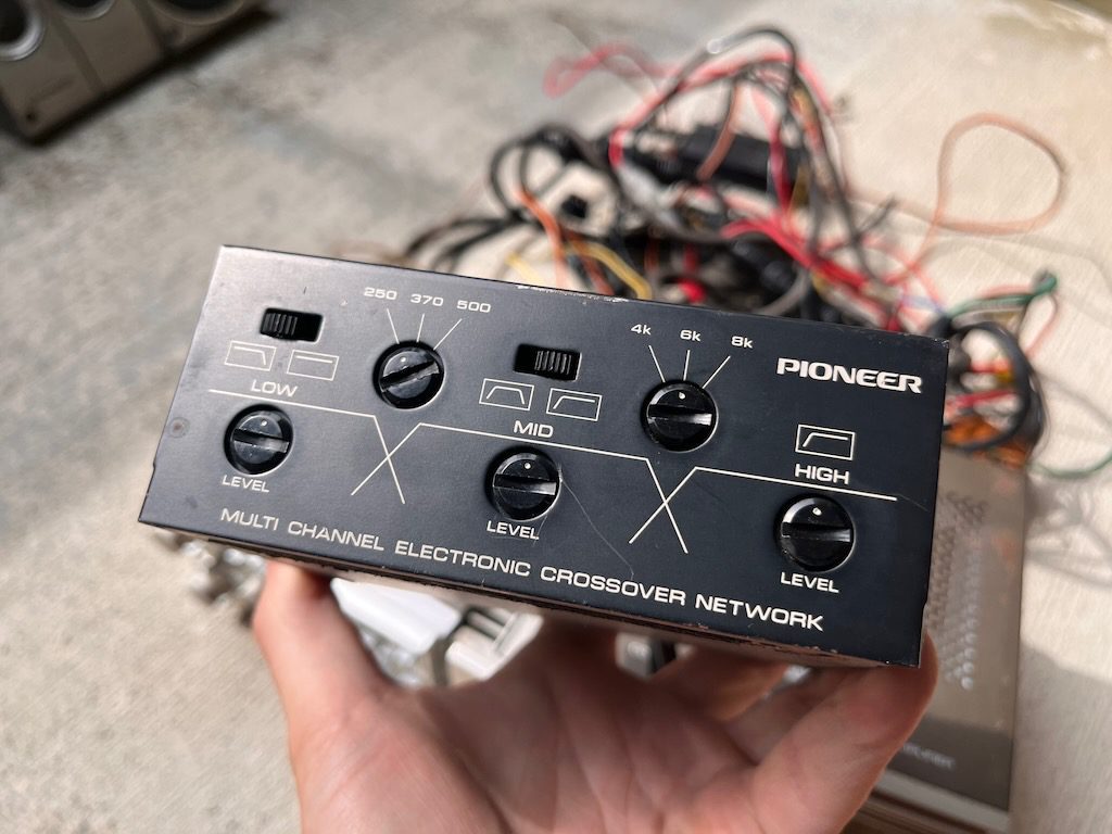 Close-up of a vintage Pioneer multi-channel electronic crossover network held in hand with wires in the background.