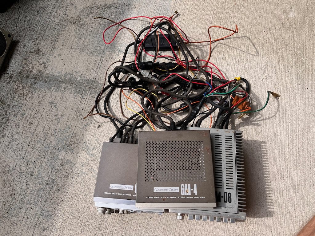Vintage Lonesome Carboy GM-4 and GM-D8 car stereo amplifiers with wiring on the cement ground.