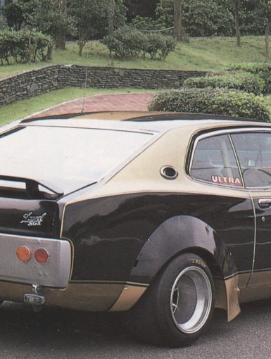 Vintage customized Eizo car with Ultra and E.YAZAWA decals parked in a green park with stone wall.