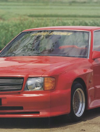 Red Koenig Specials car with sporty design and wide body kit, parked outdoor near a green field.