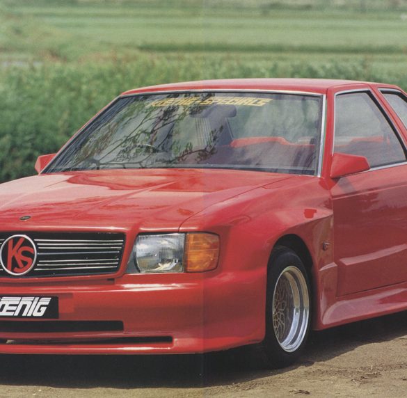 Red Koenig Specials car with sporty design and wide body kit, parked outdoor near a green field.