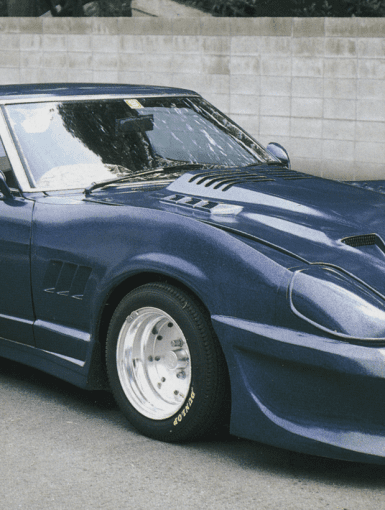 Modified blue Nissan 280ZX sports car with wide fenders, large rear wing, and custom body kit parked near concrete wall.