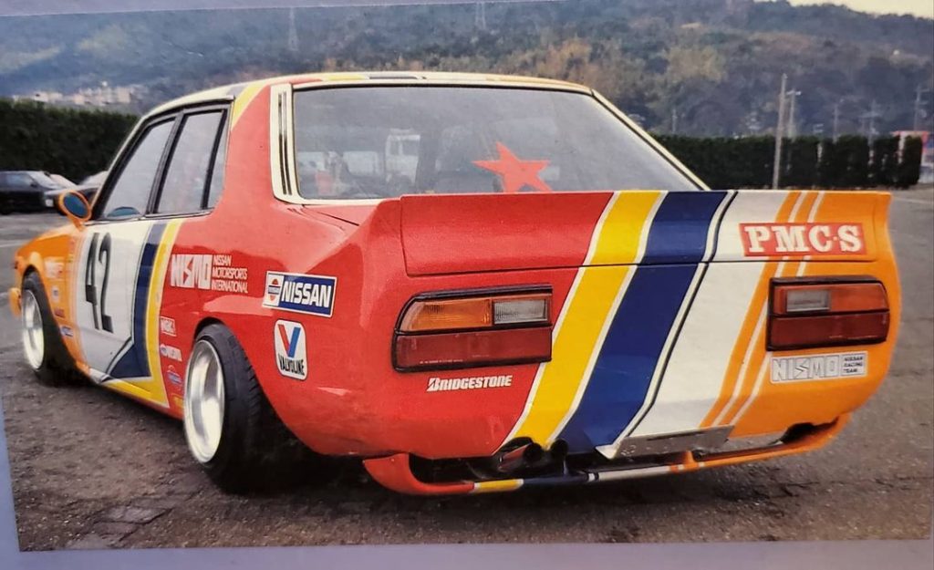 Rear view of a vintage Nissan race car with colorful stripes and sponsor logos, ready for the track.