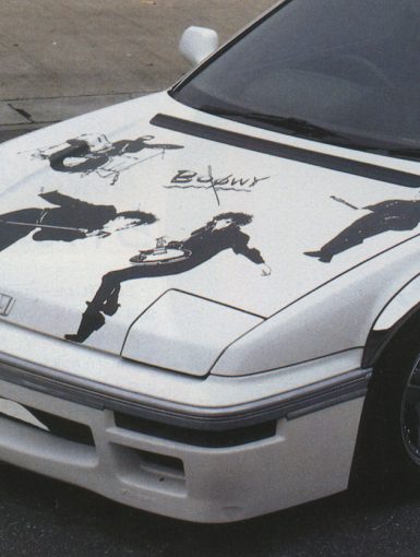 White Honda car with Boøwy band graphics on hood, Japanese text H X T on side; street view.