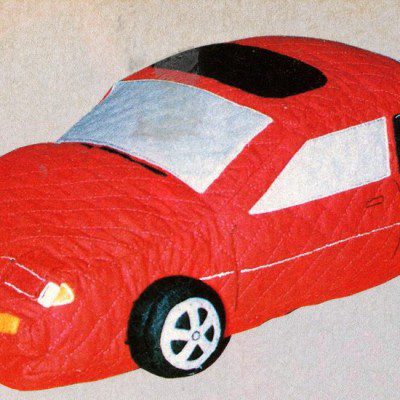 Toy red car with a quilted design, featuring realistic details on wheels and windows, on a beige background.