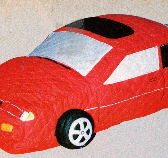 Toy red car with a quilted design, featuring realistic details on wheels and windows, on a beige background.