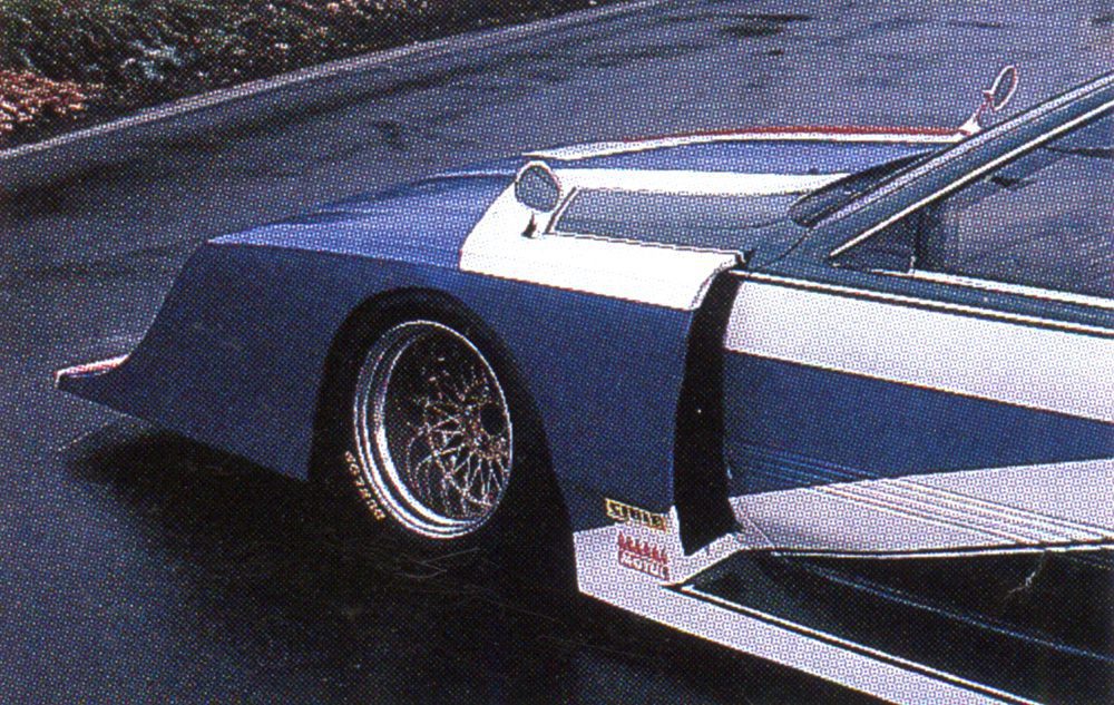 Close-up of blue retro-futuristic car with sleek design and alloy wheels on a wet road.