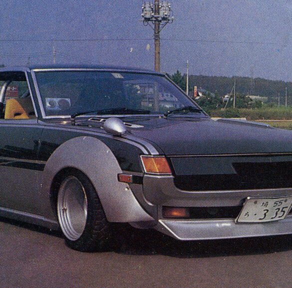 Vintage modified car with wide fenders and sleek design parked on a road with landscape in background.