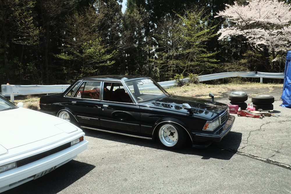 Classic Toyotas parked outdoors with spare tires and automotive tools nearby.
