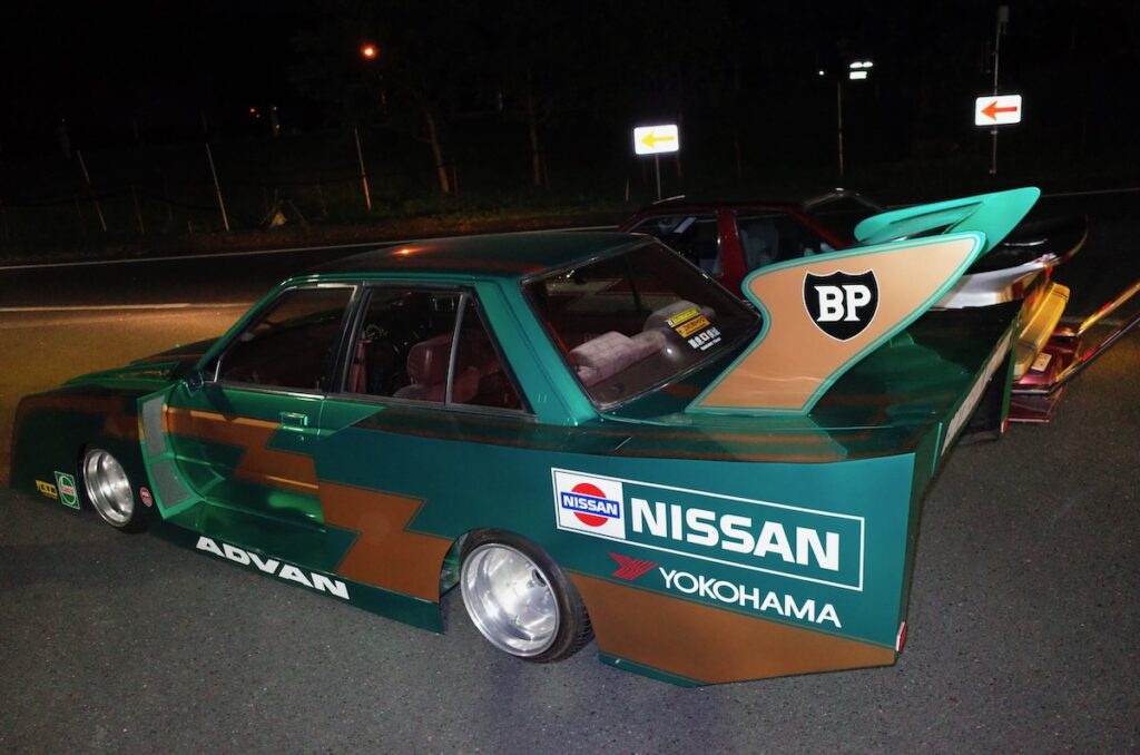 Custom Toyota race car with bold livery and large rear spoiler, photographed at night.