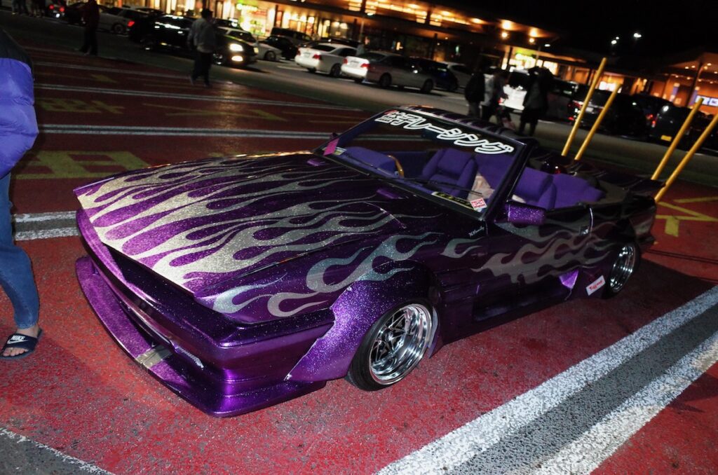 Customized purple car with flame decals in a parking lot at night.