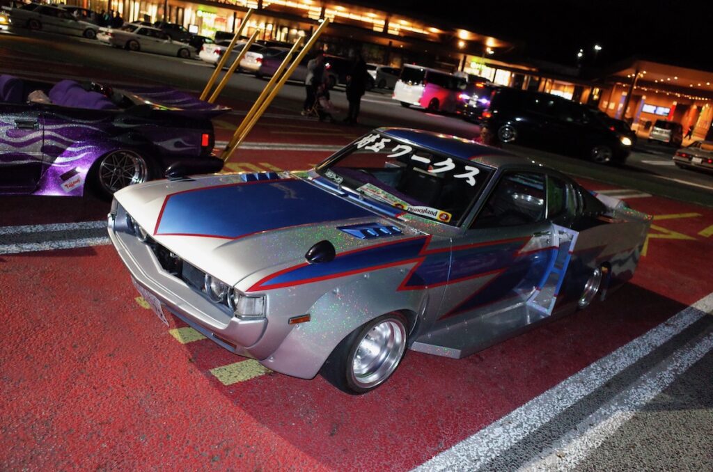 Custom vintage car with metallic paint and decals parked at night car meet.