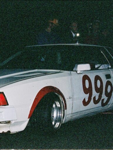 Vintage race car with number 999 painted on the side in a dark setting, showcasing classic design and headlights on.