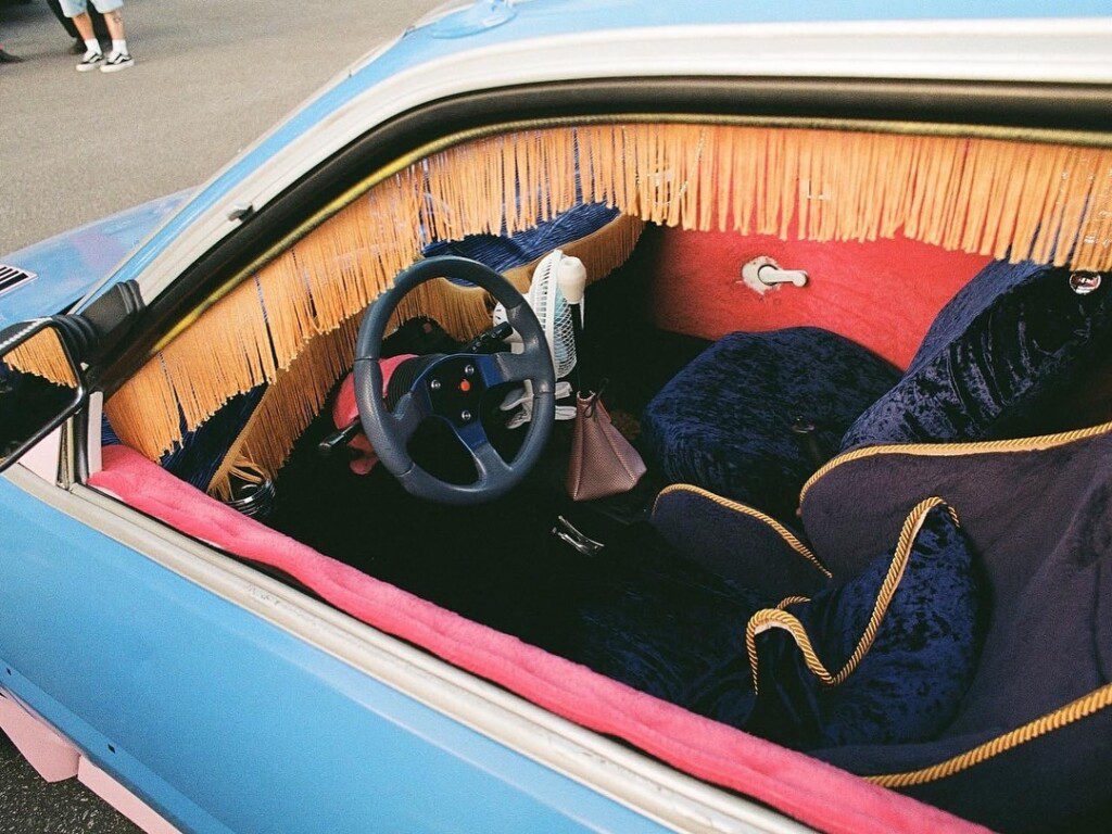 Vintage car interior with velvet seats, fringe details, and classic steering wheel in a vibrant color scheme.