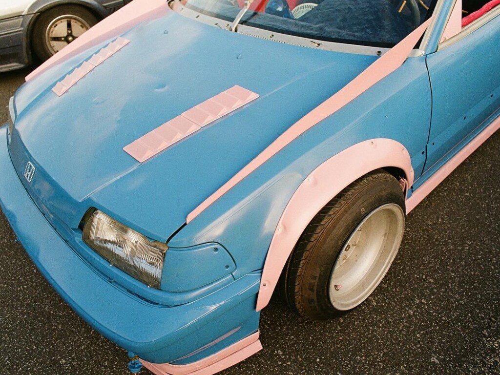 Blue and pink custom car with stylish modifications and wide tires in a parking lot, showcasing unique design elements.