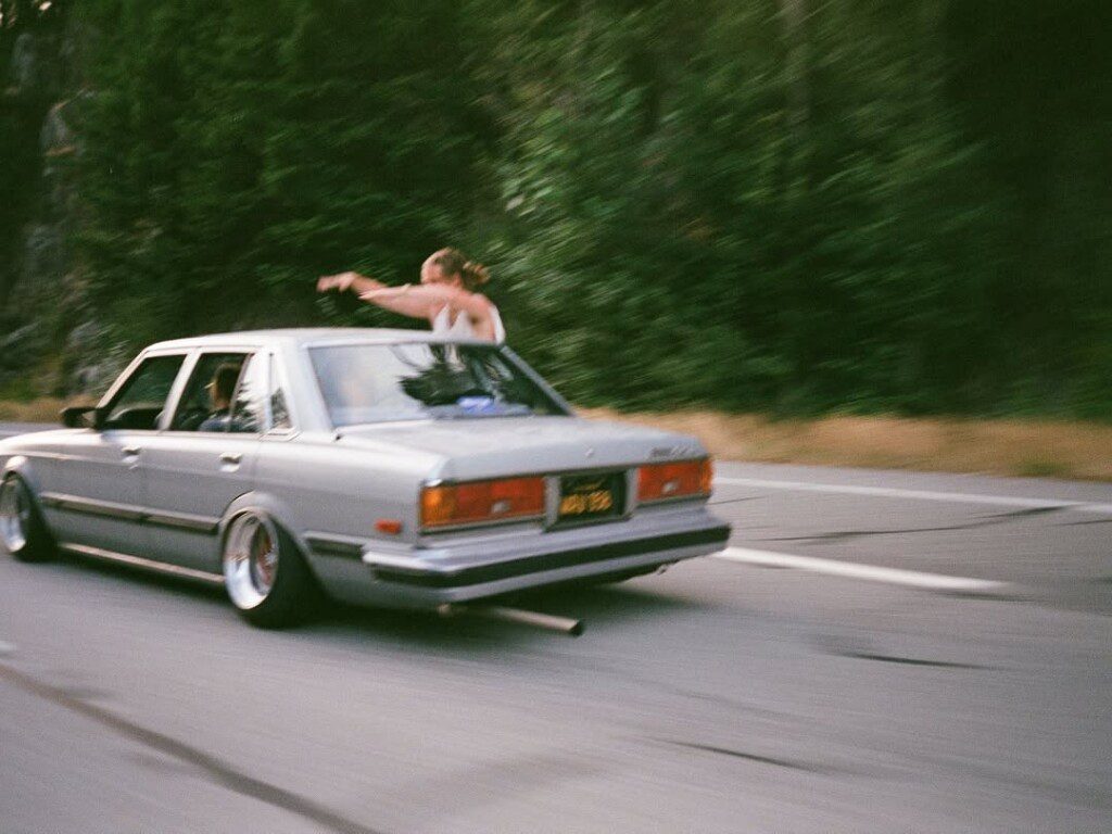 Classic car driving on a forest road with people having fun, woman leaning out of window, enjoying the ride.