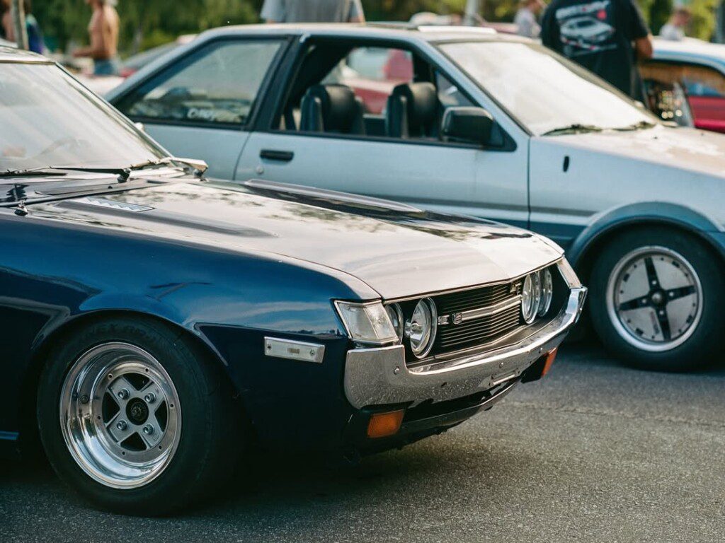 Vintage blue car parked next to a silver car at an automotive gathering.