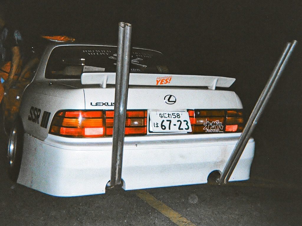 Lowered Lexus car with widebody kit and unique exhaust pipes in a night setting.