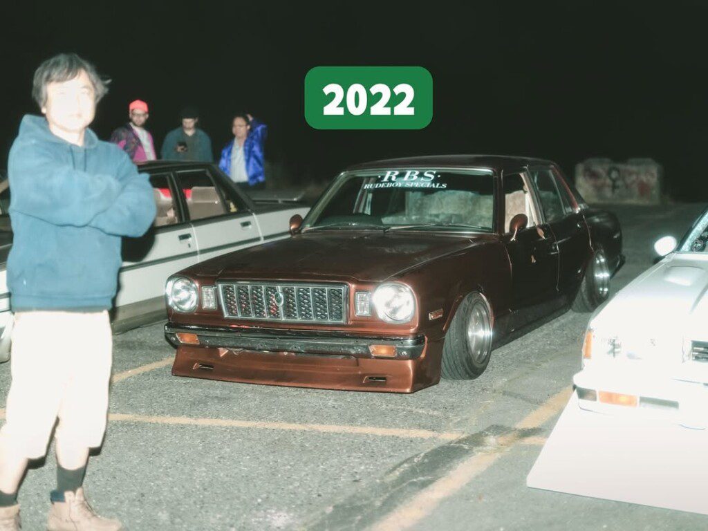 Classic car meetup 2022, vintage brown car parked at night with group of people.