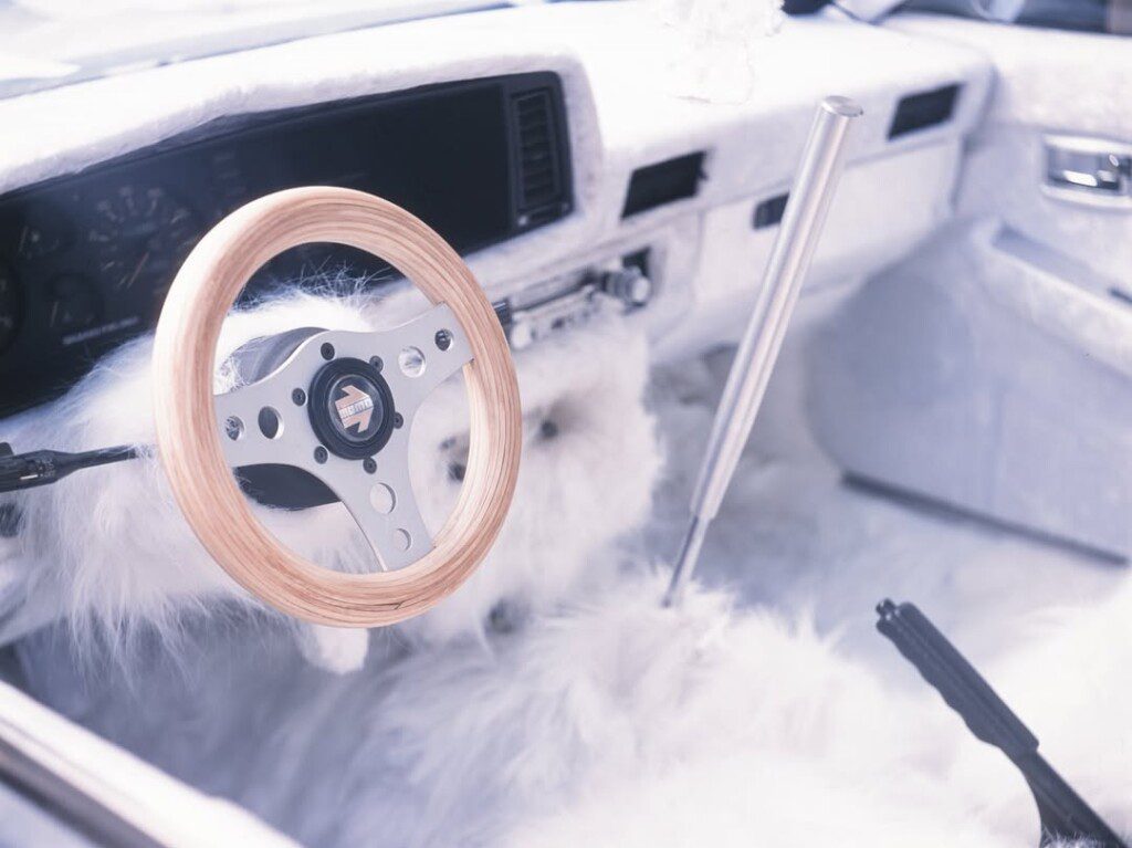 Luxurious car interior with plush fur seats and a wooden steering wheel, showcasing unique and stylish design.
