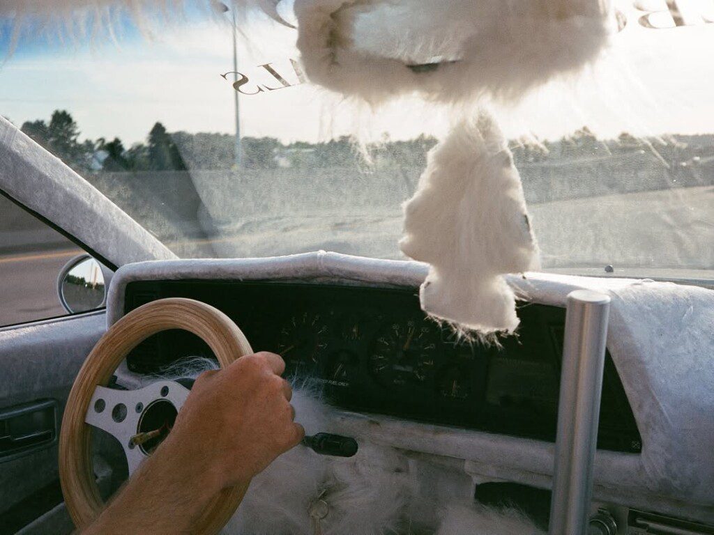 Fuzzy car interior with wooden steering wheel and fluffy air freshener, emphasizing unique vehicle customization.