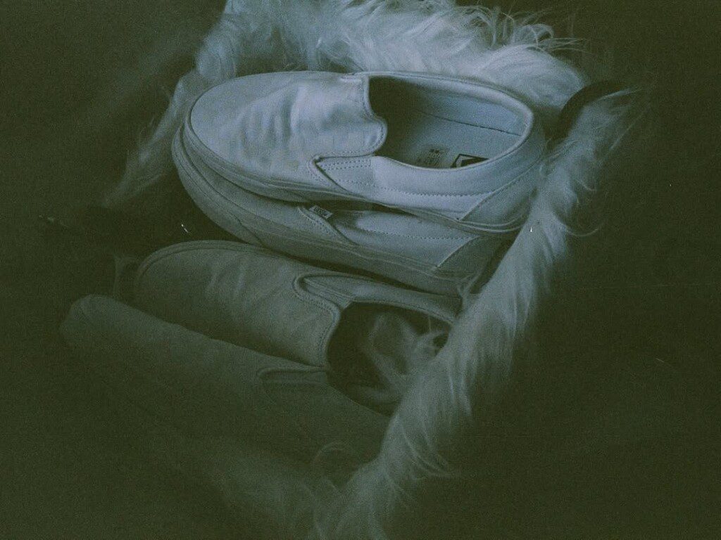 White slip-on sneakers resting on a furry surface, artistically captured in dim lighting.