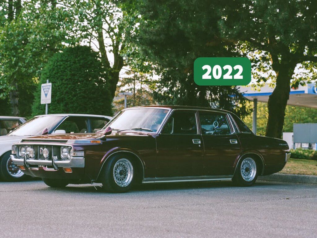 Classic dark brown car parked outdoors, trees in background, 2022 label in corner. Vintage vehicle display.