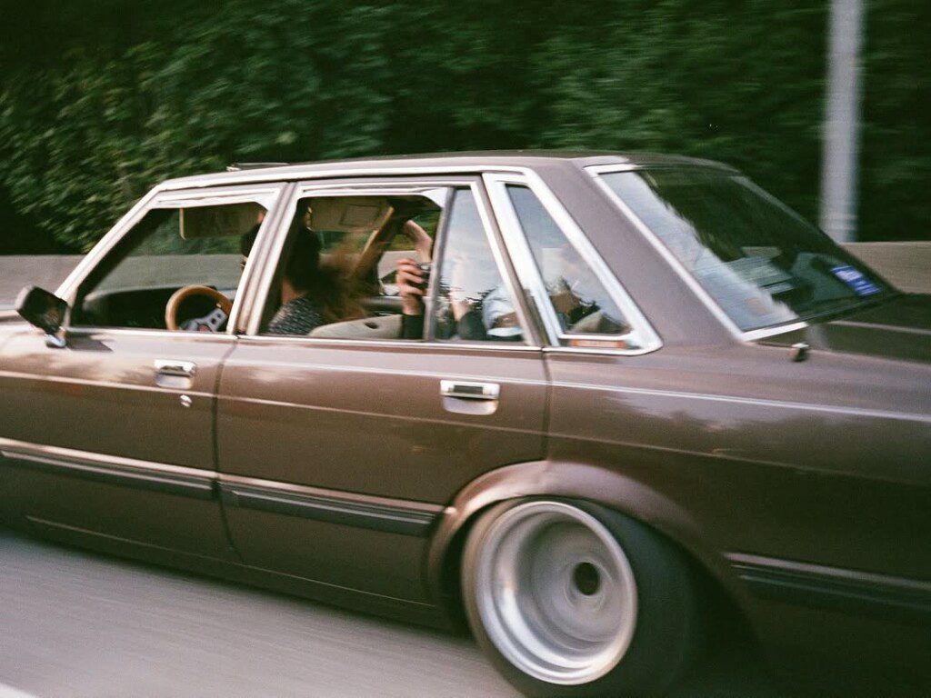 Vintage brown car speeding on highway with a blurred passenger capturing a photo through the window.