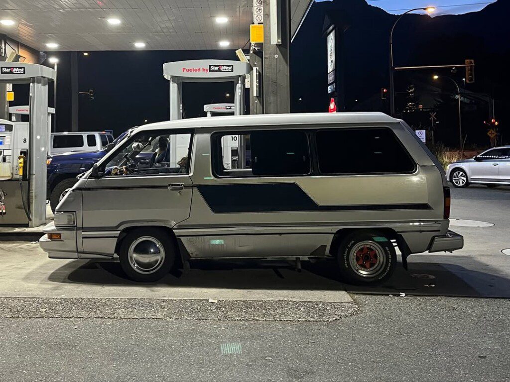 Silver van parked at a gas station at night, illuminated by overhead lights, with mountain silhouette in the background.