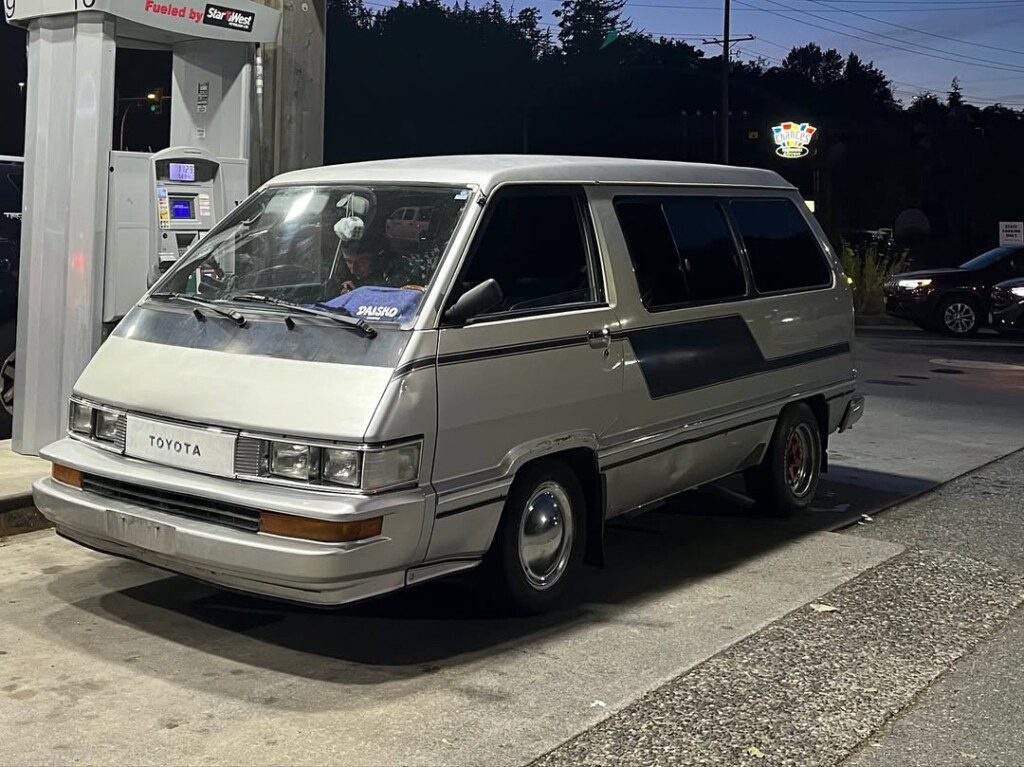 Vintage Toyota van at gas station at night, parked by the pump, with trees silhouetted in the background.