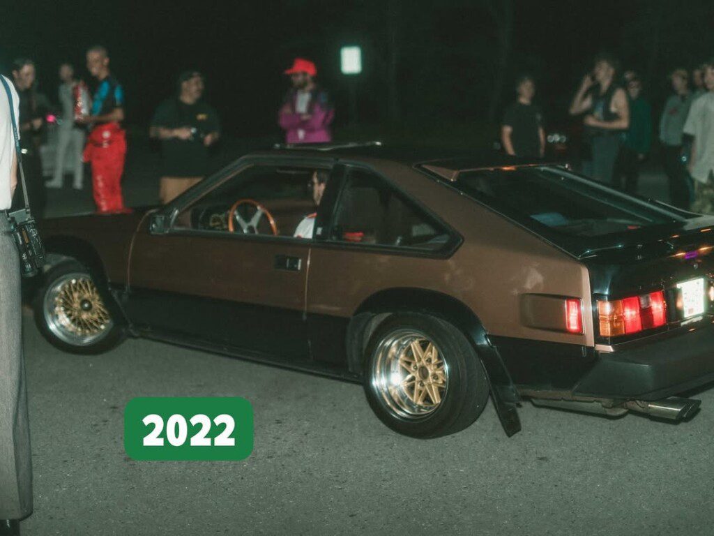 Vintage car with bronze wheels and a black hood at a night gathering, labeled 2022.