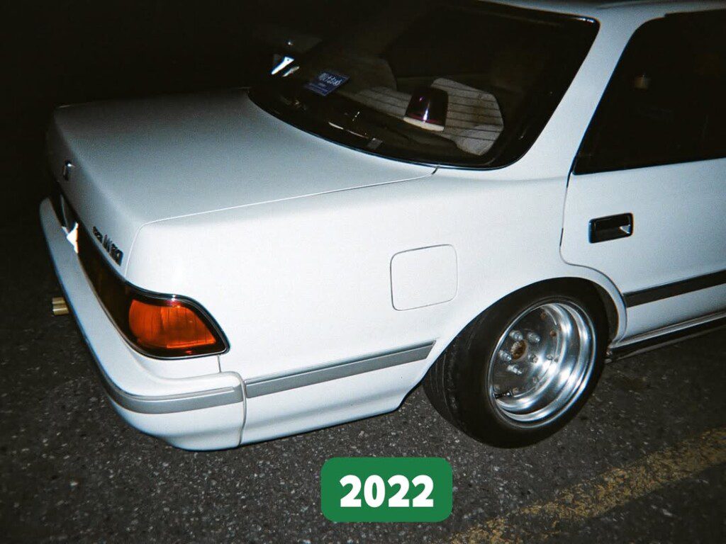 Vintage white sedan with custom wheels, rear view, parked on asphalt at night, labeled 2022.