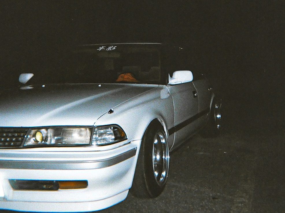 Vintage silver car with custom wheels at night, showcasing sleek headlights and a sporty design.