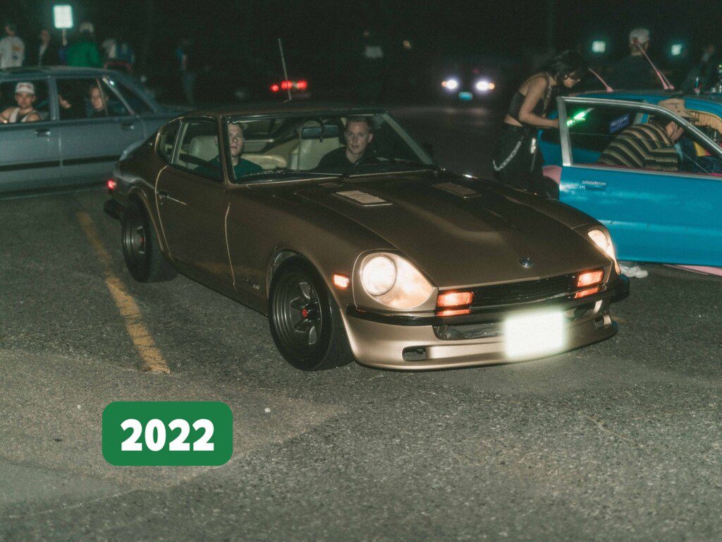 Vintage car meetup 2022 featuring a bronze classic Datsun Z in a dimly lit parking area.