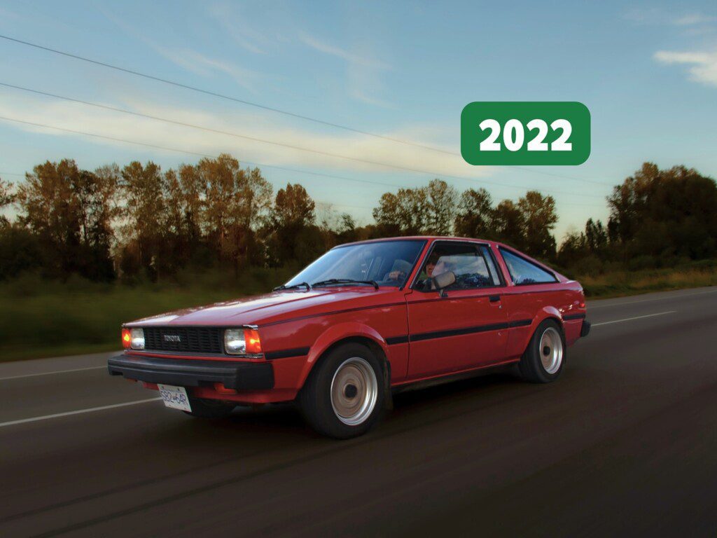 Vintage red car driving on a highway with scenic trees in the background, marked with 2022.