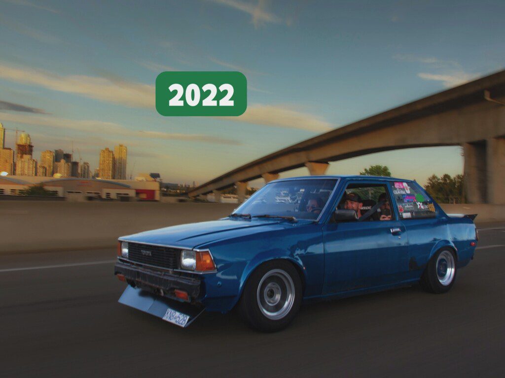 Vintage blue car driving with cityscape and overpass in background, labeled 2022.