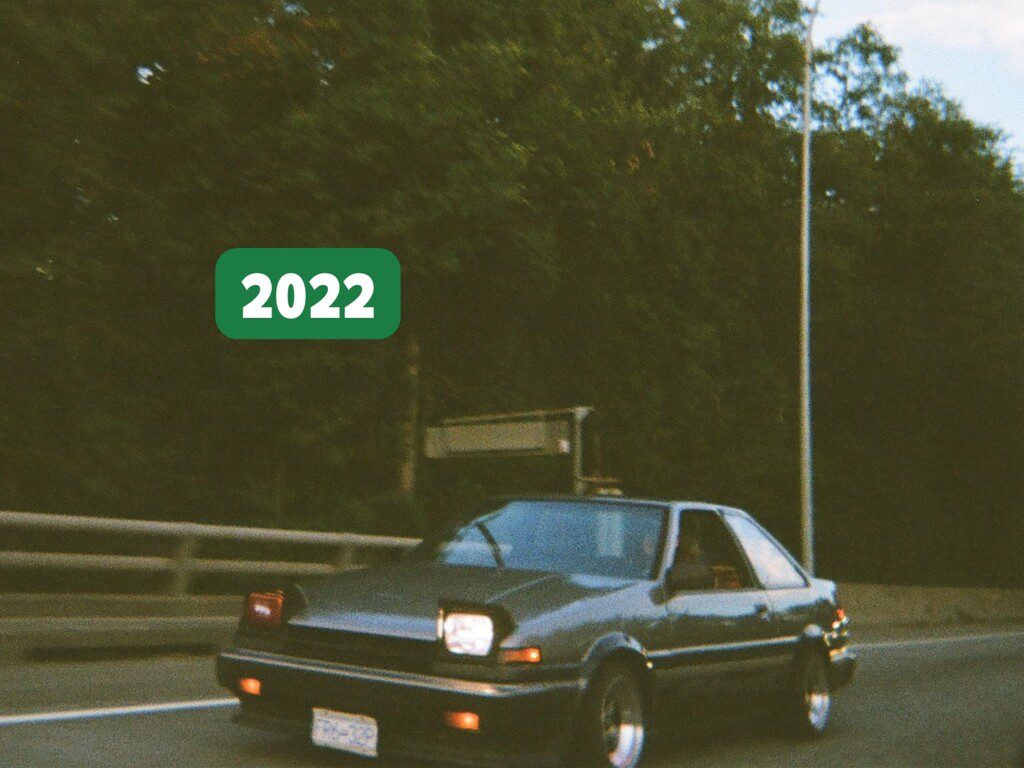 Vintage car driving on a road with trees in the background, labeled 2022. Retro style photography captures nostalgia.