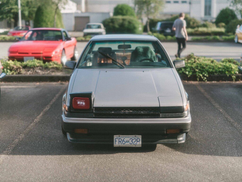 Front view of a classic gray car with a unique pop-up headlight in a parking lot on a sunny day.