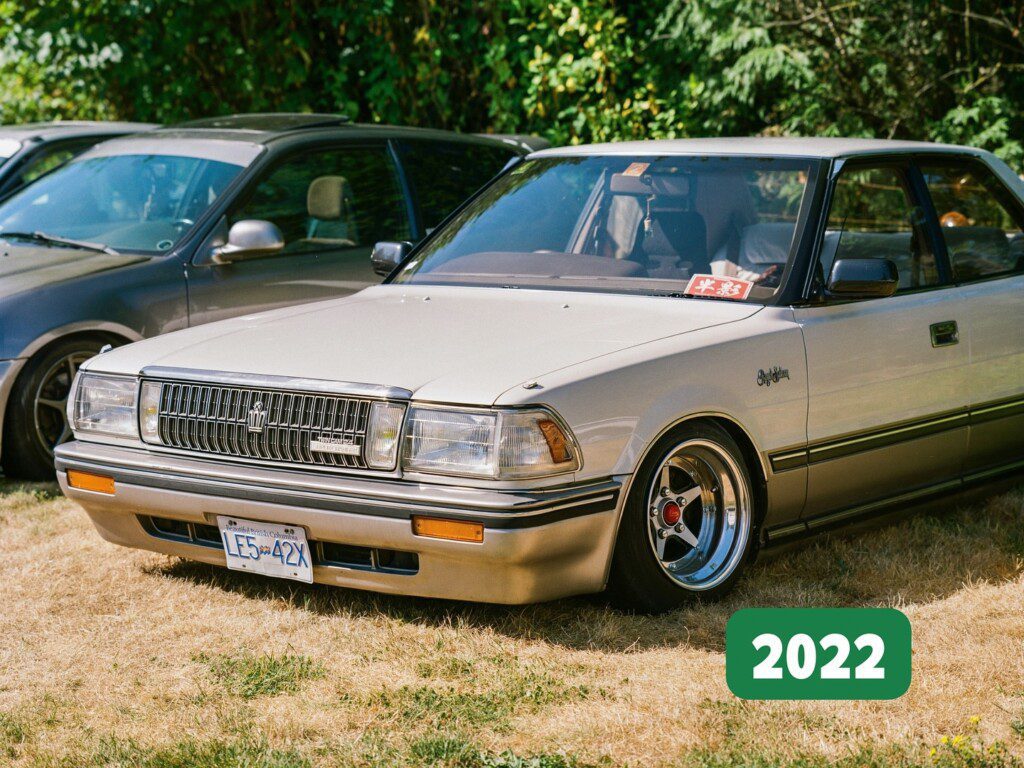 Classic beige luxury sedan in a park, featuring chrome rims and classic badge, sunny day, 2022.