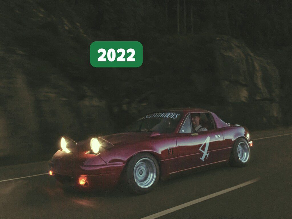 Red sports car with pop-up headlights driving at night, marked 2022 with a driver inside.
