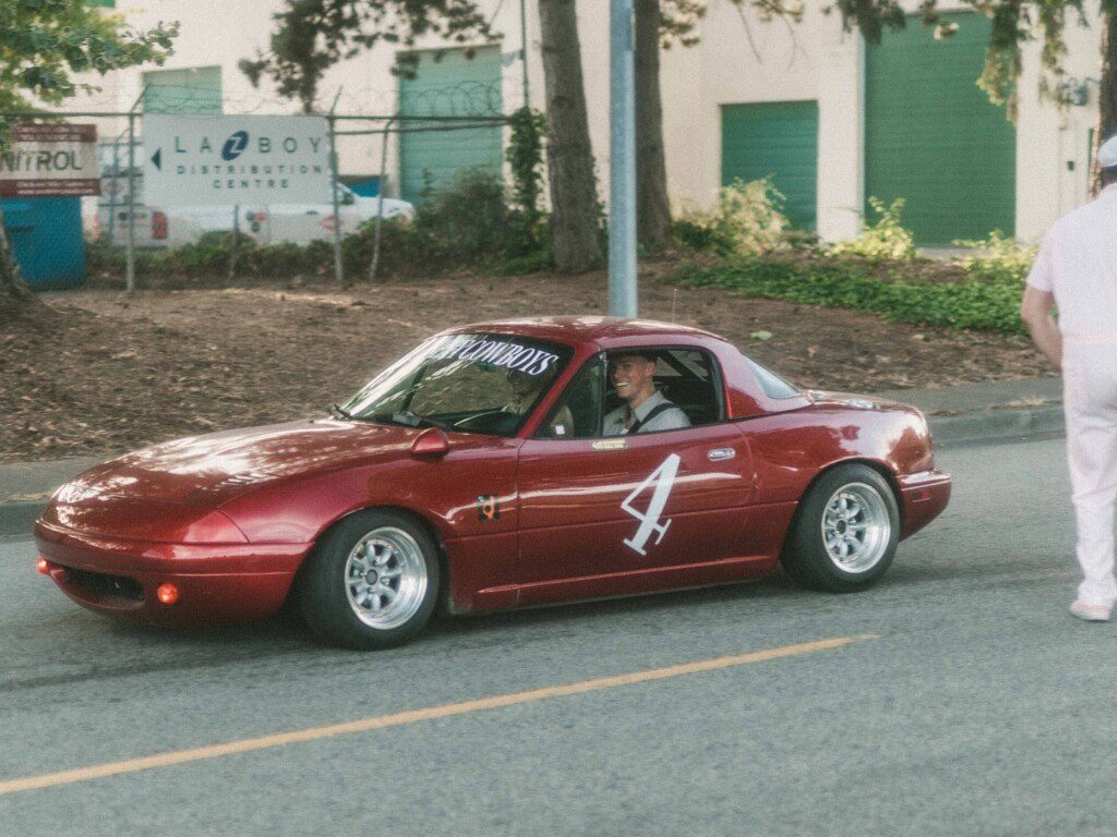 Red sports car with number 4 decal on the street, smiling driver inside.